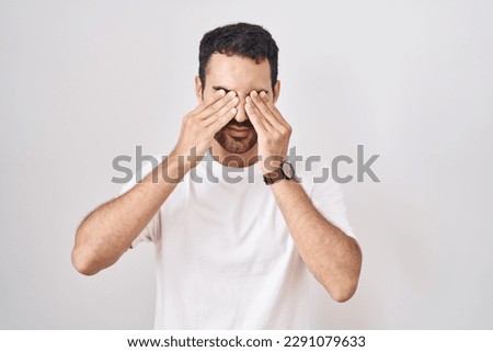 Handsome hispanic man standing over white background rubbing eyes for fatigue and headache, sleepy and tired expression. vision problem 