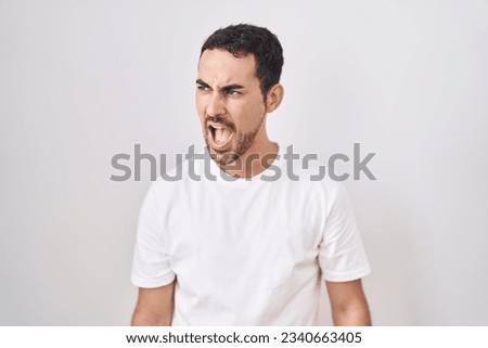 Handsome hispanic man standing over white background angry and mad screaming frustrated and furious, shouting with anger. rage and aggressive concept. 