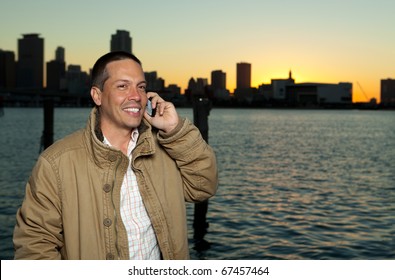 Handsome hispanic man in an urban lifestyle pose talking on a mobile phone with a downtown skyline in the background in the late afternoon at sunset. - Powered by Shutterstock