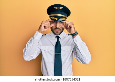 Handsome Hispanic Man Wearing Airplane Pilot Uniform Trying To Open Eyes With Fingers, Sleepy And Tired For Morning Fatigue 