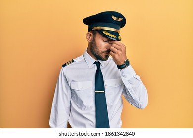 Handsome Hispanic Man Wearing Airplane Pilot Uniform Tired Rubbing Nose And Eyes Feeling Fatigue And Headache. Stress And Frustration Concept. 