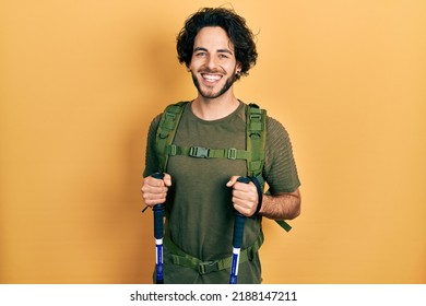 Handsome Hispanic Man Wearing Backpack Holding Trekking Poles Smiling With A Happy And Cool Smile On Face. Showing Teeth. 