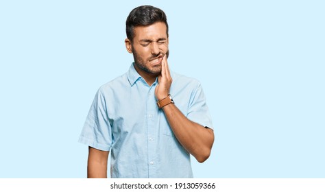 Handsome hispanic man wearing casual clothes touching mouth with hand with painful expression because of toothache or dental illness on teeth. dentist 