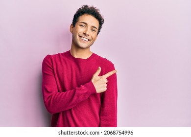 Handsome hispanic man wearing casual clothes over pink background smiling cheerful pointing with hand and finger up to the side  - Powered by Shutterstock