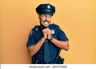 Handsome hispanic man wearing police uniform laughing nervous and excited with hands on chin looking to the side 