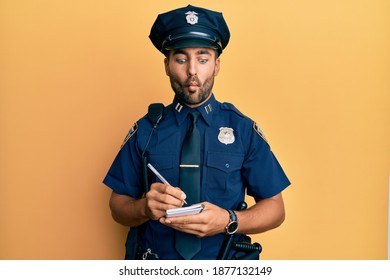 Handsome hispanic man wearing police uniform writing traffic fine making fish face with mouth and squinting eyes, crazy and comical. 