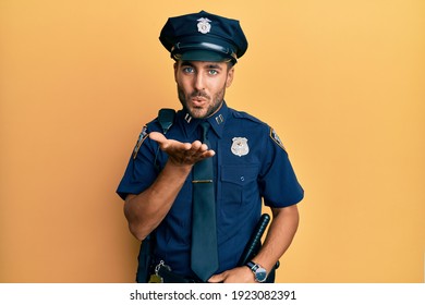 Handsome hispanic man wearing police uniform looking at the camera blowing a kiss with hand on air being lovely and sexy. love expression. 