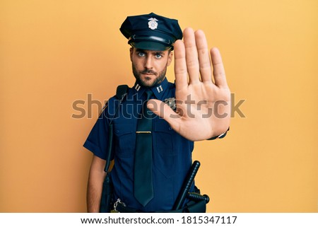 Handsome hispanic man wearing police uniform doing stop sing with palm of the hand. warning expression with negative and serious gesture on the face. 