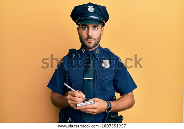 Handsome hispanic man wearing police uniform
writing traffic fine relaxed with serious expression on face.
simple and natural looking at the camera.
