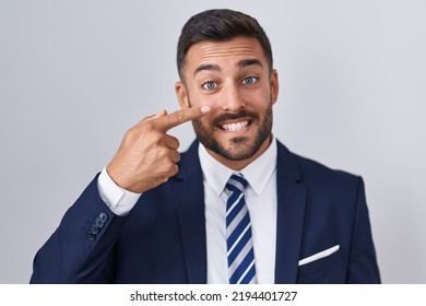 Handsome Hispanic Man Wearing Suit And Tie Pointing With Hand Finger To Face And Nose, Smiling Cheerful. Beauty Concept 