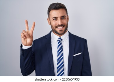 Handsome hispanic man wearing suit and tie showing and pointing up with fingers number two while smiling confident and happy. 