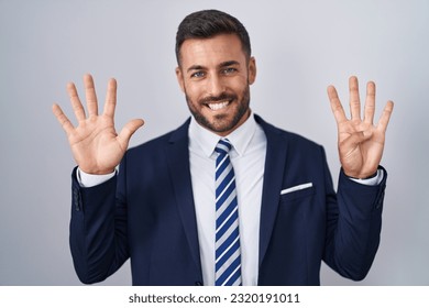 Handsome hispanic man wearing suit and tie showing and pointing up with fingers number nine while smiling confident and happy. 