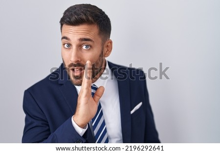 Handsome hispanic man wearing suit and tie hand on mouth telling secret rumor, whispering malicious talk conversation 