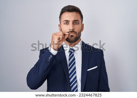 Handsome hispanic man wearing suit and tie mouth and lips shut as zip with fingers. secret and silent, taboo talking 