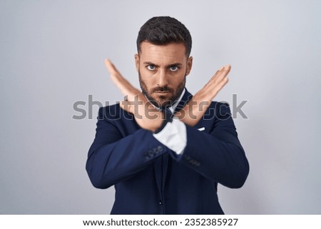 Handsome hispanic man wearing suit and tie rejection expression crossing arms doing negative sign, angry face 