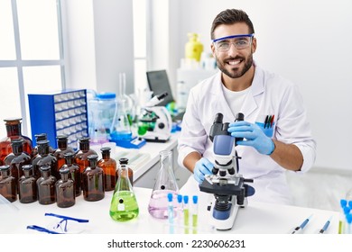 Handsome hispanic man working at scientist laboratory looking positive and happy standing and smiling with a confident smile showing teeth  - Shutterstock ID 2230606231