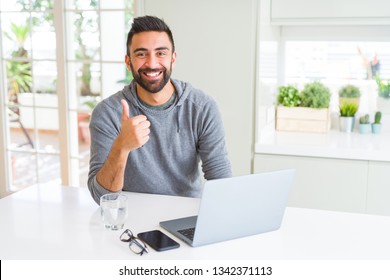 Handsome hispanic man working using computer laptop happy with big smile doing ok sign, thumb up with fingers, excellent sign