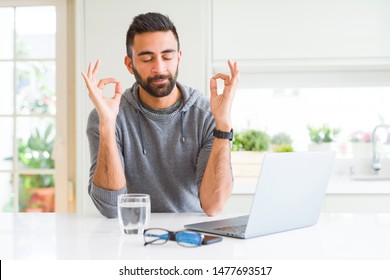 Handsome hispanic man working using computer laptop relax and smiling with eyes closed doing meditation gesture with fingers. Yoga concept.