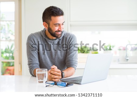 Handsome hispanic man working using computer laptop looking away to side with smile on face, natural expression. Laughing confident.
