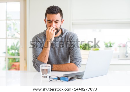 Handsome hispanic man working using computer laptop looking stressed and nervous with hands on mouth biting nails. Anxiety problem.