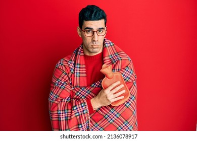 Handsome hispanic man wrapped in a winter blanket holding hot water bag depressed and worry for distress, crying angry and afraid. sad expression. 