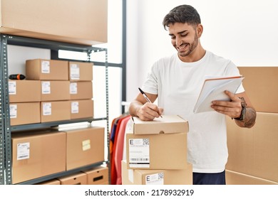 Handsome hispanic man writing address on cardboard boxes at e-commerce store - Shutterstock ID 2178932919