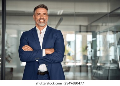 Handsome hispanic senior business man with crossed arms smiling aside. Indian or latin confident mature good looking middle age leader male businessman on blur office background with copy space. - Powered by Shutterstock