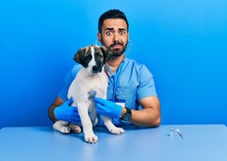 Handsome Hispanic Veterinary Man With Beard Checking Dog Health Using Stethoscope Skeptic And Nervous, Frowning Upset Because Of Problem. Negative Person. 