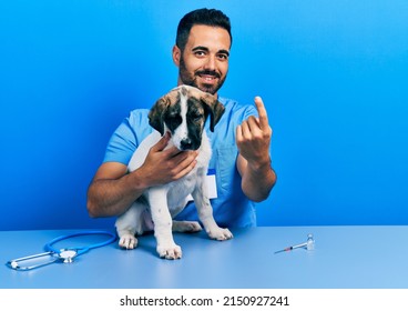 Handsome Hispanic Veterinary Man With Beard Checking Dog Health Beckoning Come Here Gesture With Hand Inviting Welcoming Happy And Smiling 