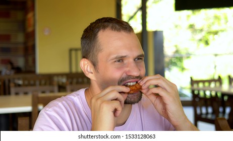 Handsome Hungry Guy Eating Grilled Chicken Wings In Fast Food Cafe. Close-up.