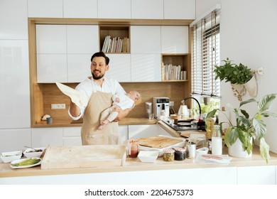 Handsome Husband Holding Adorable Lovely Son In Arms Throwing Up Kneading Homemade Pizza Baking Preparing Surprise For Family Dinner.