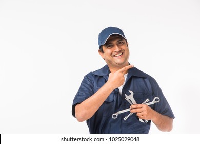 Handsome Indian Auto Mechanic presenting something or showing empty biz card while holding tools like spanner in one hand - Powered by Shutterstock