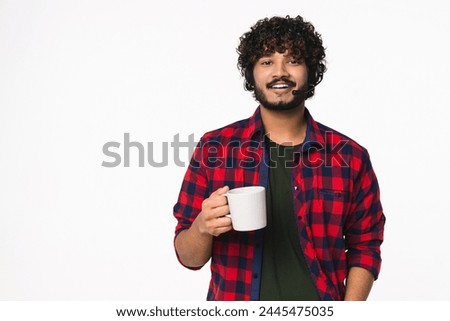 Handsome Indian dispatcher in headset drinking hot coffee isolated over white background. Cheerful Hindi IT-support manager hotline worker holding cup mug with hot beverage