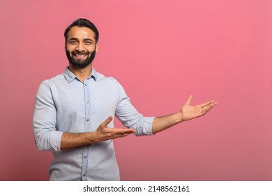 Handsome Indian guy points palms at empty copy space isolated on pink background. Cheerful multiracial bearded man in casual jeans shirt presenting novelty, advertising concept - Shutterstock ID 2148562161