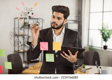 Handsome indian man in formal suit holding digital tablet while writing brilliant ideas on glass wall at corporate office. Concept of business, people and modern gadgets. - Shutterstock ID 2159766085