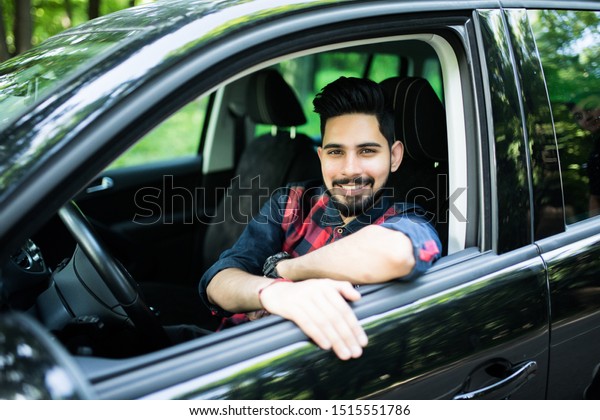 A handsome Indian man in a saloon car outside\
in countryside