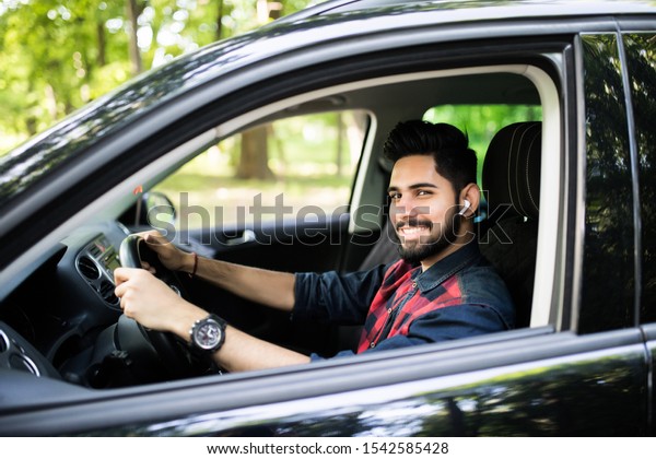 A handsome Indian man in a saloon car outside\
in countryside