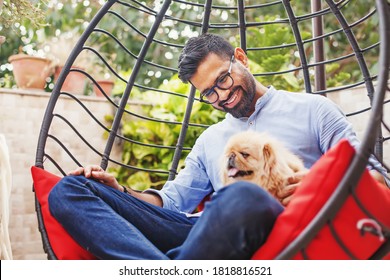 Schöner Indianer, der mit seinem süßen kleinen Hund auf dem Hängestuhl im Garten sitzt