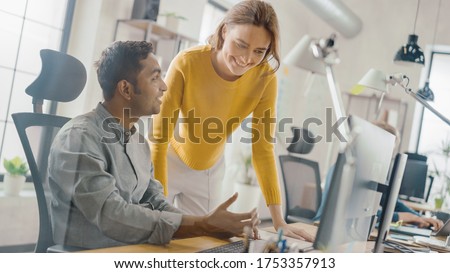 Handsome Indian Professional Sitting at His Desk Working on Laptop Computer, Young Beautiful Team Leader Gives Advice about Project Details. Office with Young Professionals Work. Dutch Angle.