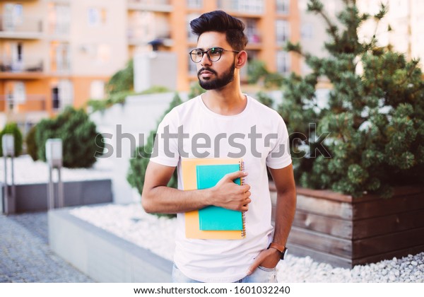 Handsome indian student man read notebooks while\
standing on the street