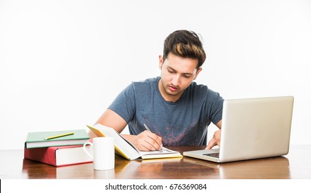 Handsome Indian/Asian College Student Studying On Laptop Or From Many Books Kept Over Table With Coffee Mug, Over Plain White Background