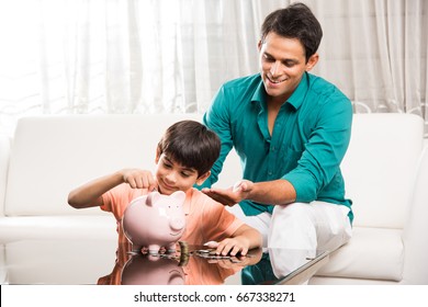 Handsome Indian/asian Father Teaching Importance Of Saving To His Kid At Home With Piggy Bank