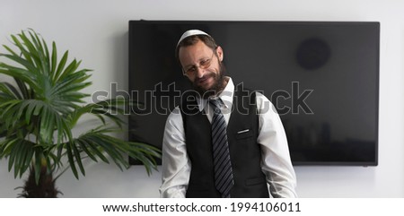 Handsome jewish Businessman in glasses looking down. Jew man in a white shirt, business suit and national hat kippah smiling in a conference, meeting room or home office. Senior orthodox Jewish man