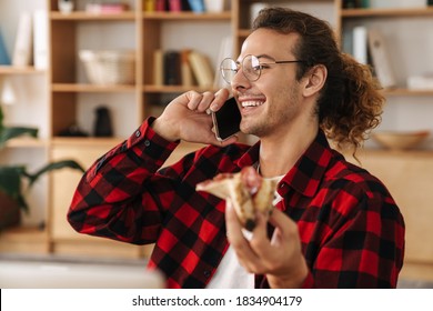 Handsome Joyful Guy Talking On Cellphone While Eating Pizza At Office