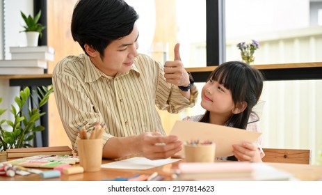 Handsome And Kind Asian Male Art Teacher Giving A Thumbs Up To His Adorable Young Student. Asian Dad And Daughter Enjoys Painting Together.