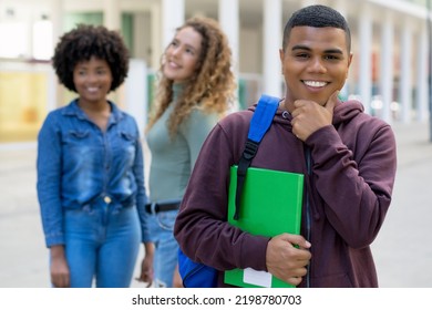 Handsome Latin American Male Student With Backpack And Group Of International Students Outdoor In Summer In City