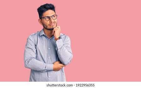 Handsome latin american young man wearing business clothes and glasses serious face thinking about question with hand on chin, thoughtful about confusing idea 