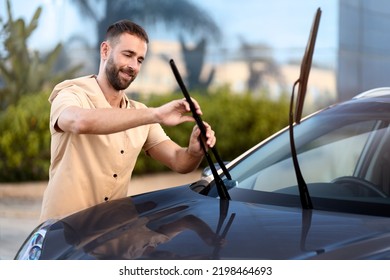 Handsome Latin Man Replace Windshield Wipers On Car Standing Outdoors. Car Service Concept 