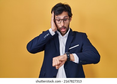 Handsome latin man standing over yellow background looking at the watch time worried, afraid of getting late 