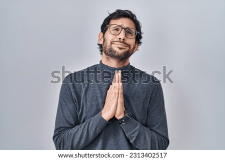 Handsome latin man standing over isolated background begging and praying with hands together with hope expression on face very emotional and worried. begging. 